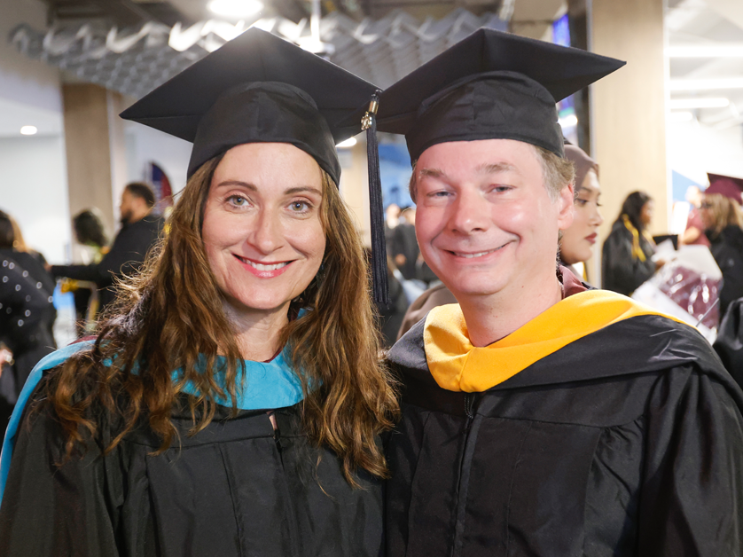 male and female graduate smiling in academic regalia