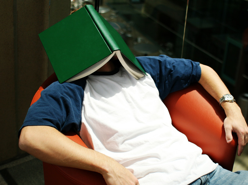 man with textbook on face lying in a chair