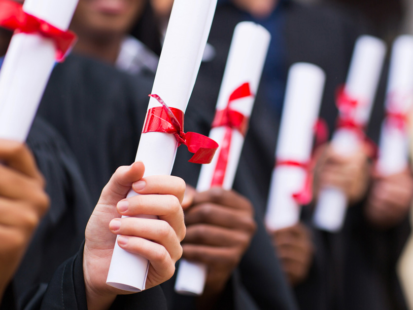close up row of graduates holding rolled up diplomas