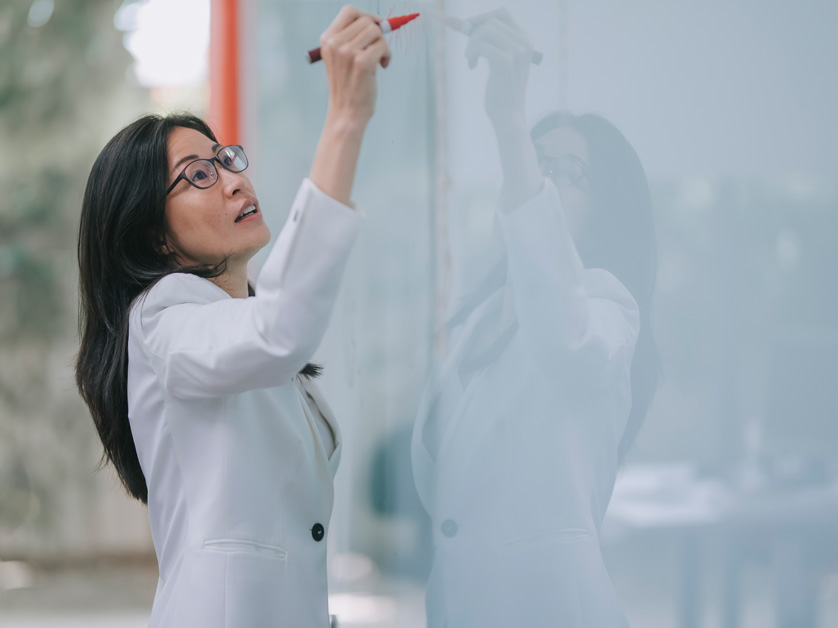 woman wearing lab coat and writing on whiteboard